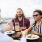 young friends on a balcony overlooking the pier, toasting drinks around a table of food