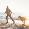 man running with dog on beach